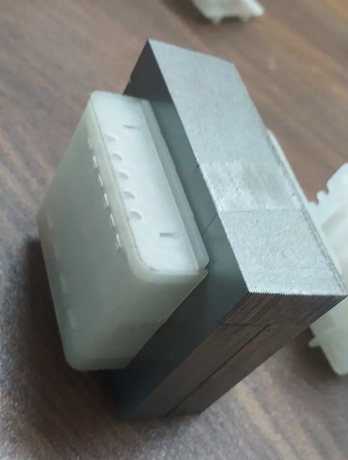 Corner view of the bobbin against the edge of the lamination stack, showing the flange, the row of terminal slots and the individual laminations