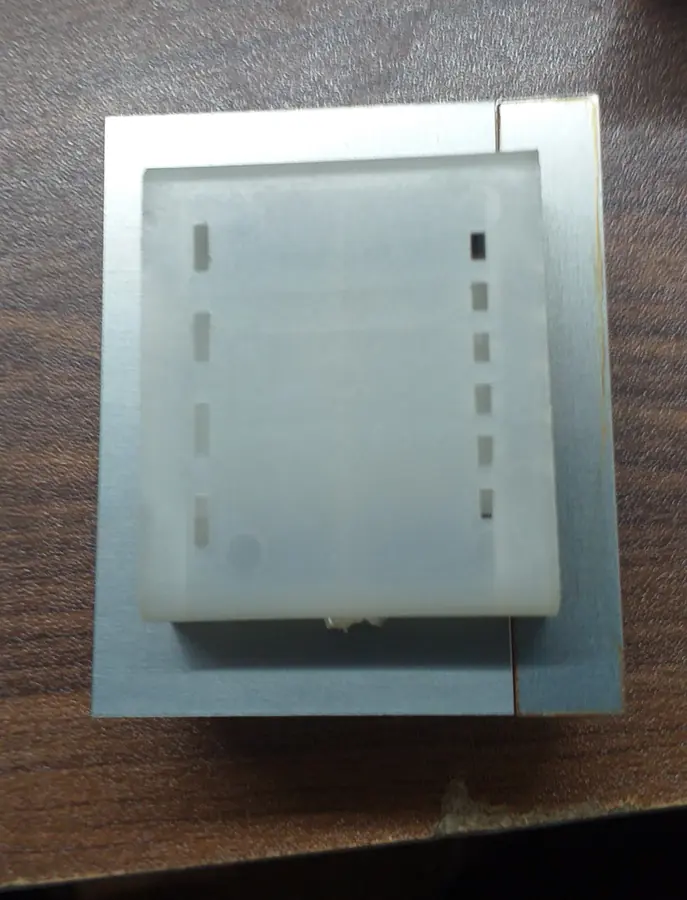 Plan view of the white moulded bobbin seated inside the window of the stacked steel laminations, terminal slots visible down both flanges