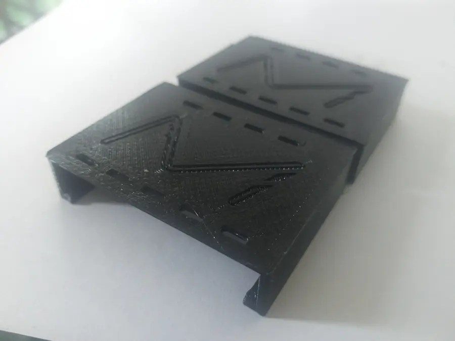Two black 3D printed end caps side by side, showing the embossed face detail and the slotted edges